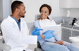 Smiling dentist and patient reviewing information on tablet