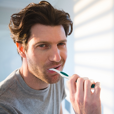 Man in grey shirt brushing his teeth
