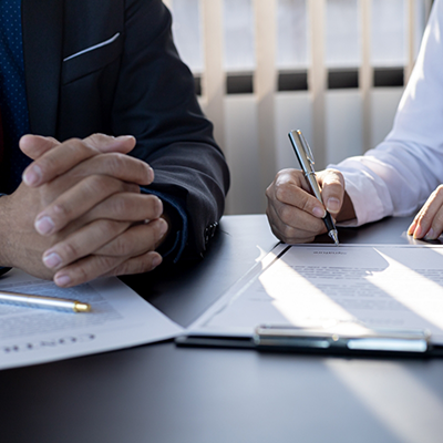 Man with hands folded while another one fills out form on clipboard