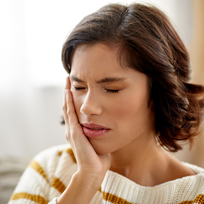 Woman in sweater rubbing jaw in pain
