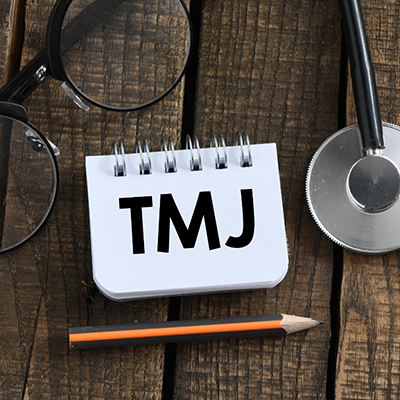 Letter TMJ on notepad on table with glasses and stethoscope