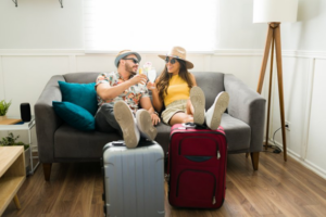 Beach-ready couple sitting on couch, using suitcases as footrests
